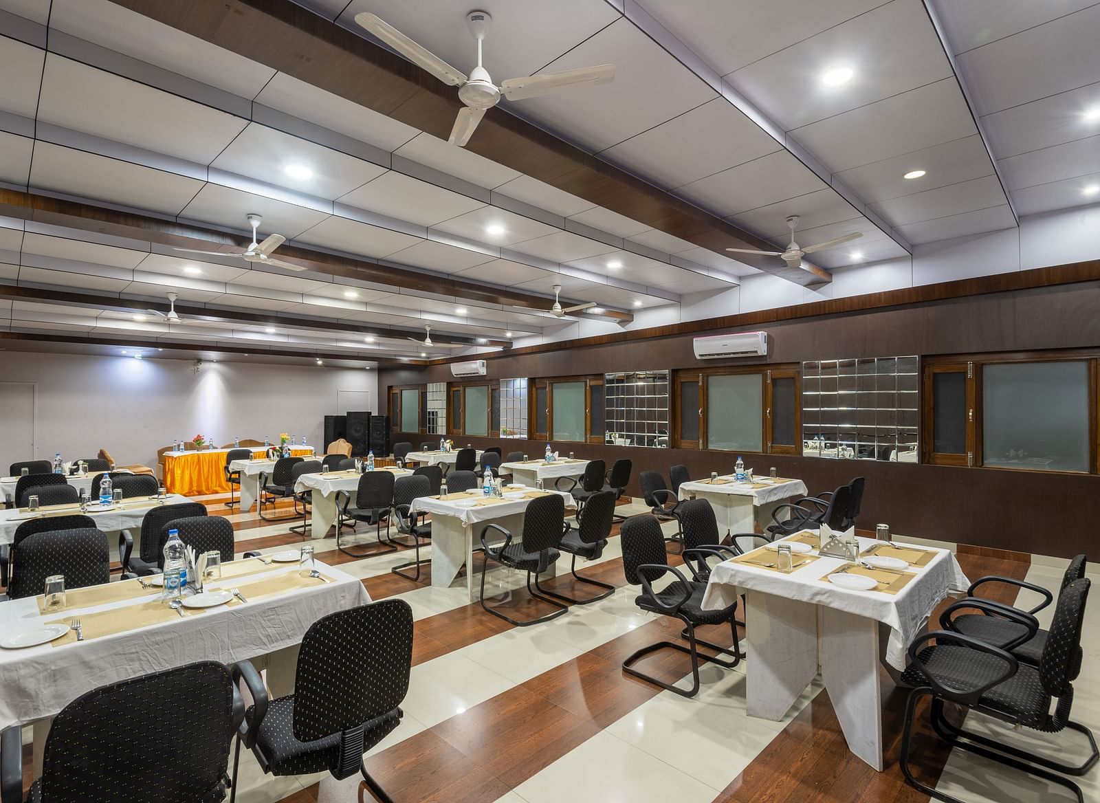 A large, well-lit conference room with rows of tables and chairs arranged for a meeting - DLS Meghavan Resort 